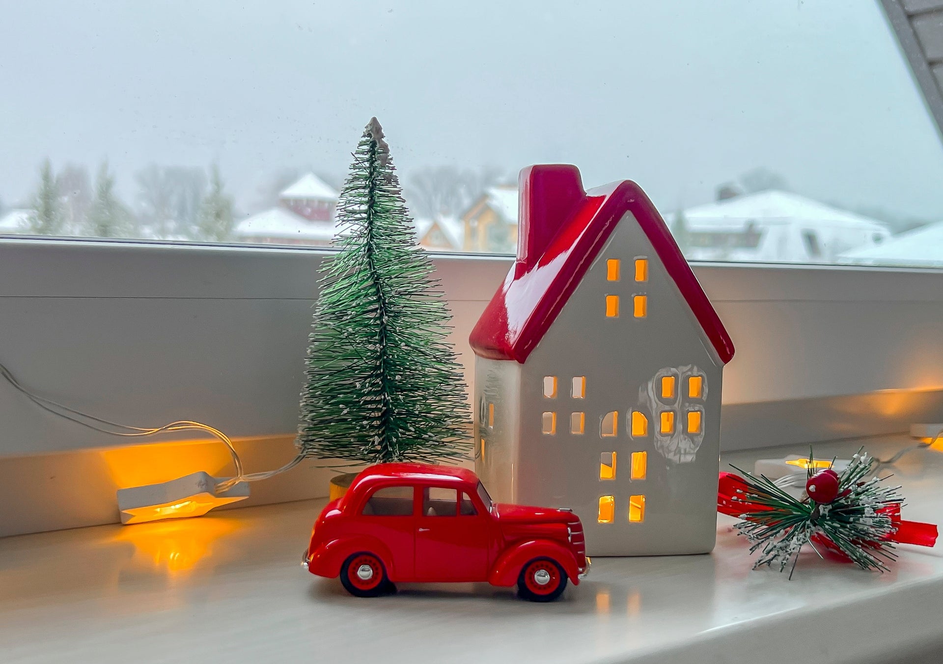 Cozy Christmas window scene with warm lights, mini house decor and snowy village background - festive, calm holiday atmosphere.