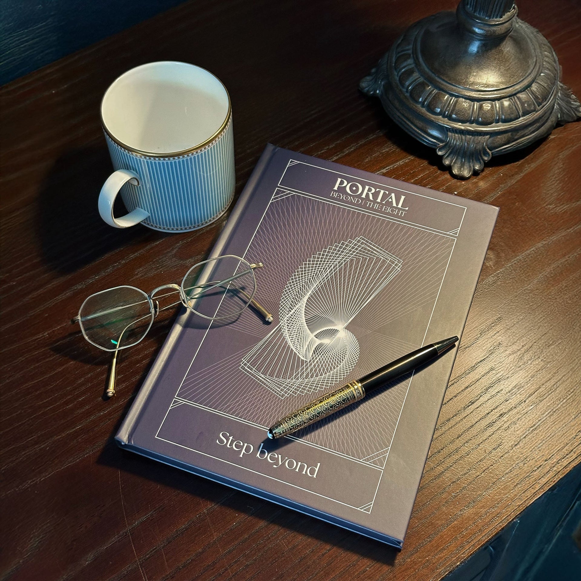 Portal hardcover notebook by The Ei8ht on a wooden table with a mug, glasses, and a pen, geometric cover design visible.